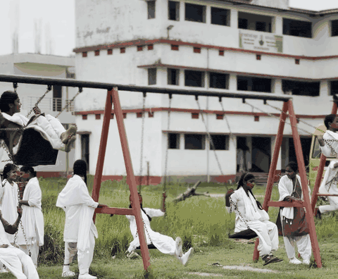 Girls on swings in the school field, with a three-storey school block and a school bus behind them